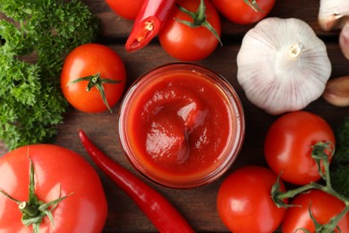 Photo of Jar of tasty ketchup and ingredients on wooden table, flat lay