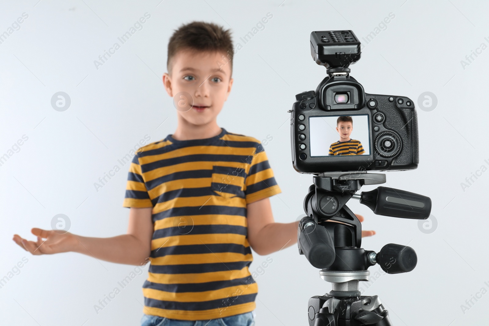 Photo of Cute little blogger recording video against white background, focus on camera