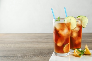 Glasses of refreshing iced tea on wooden table against light background. Space for text