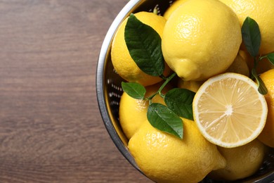 Photo of Fresh lemons and green leaves in colander on wooden table, top view. Space for text