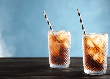 Glasses of refreshing cola with ice cubes and straws on table. Space for text