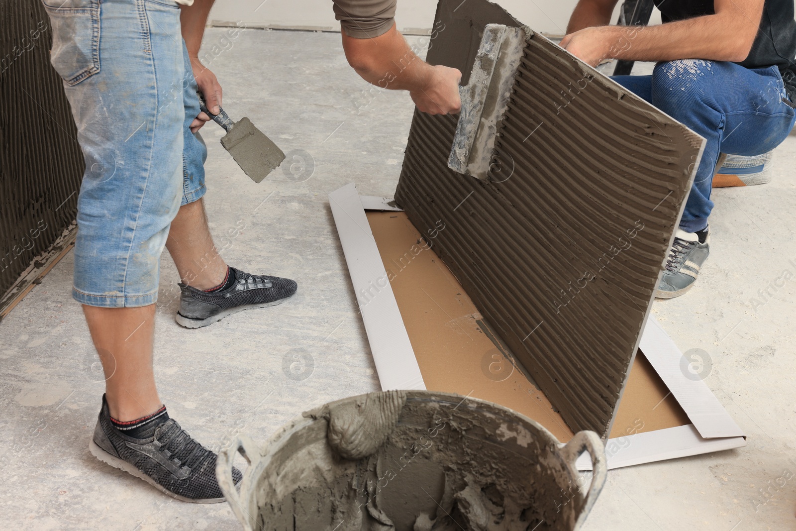 Photo of Worker spreading adhesive mix over tile with spatula, closeup