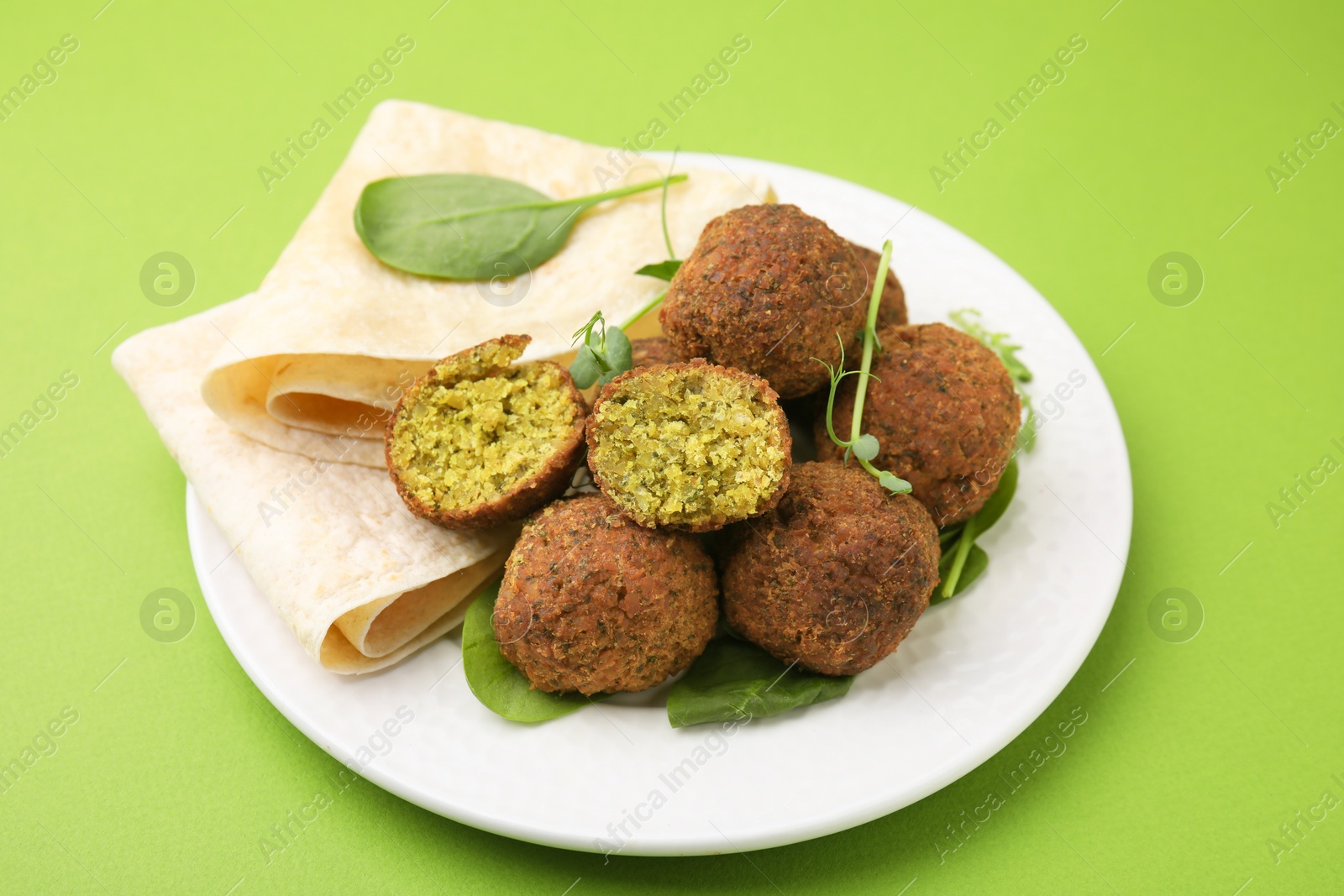 Photo of Delicious falafel balls, herbs and lavash on green background