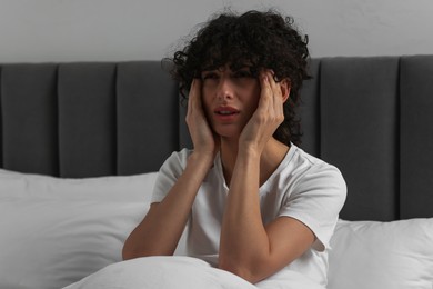 Photo of Young woman suffering from headache in bed at night
