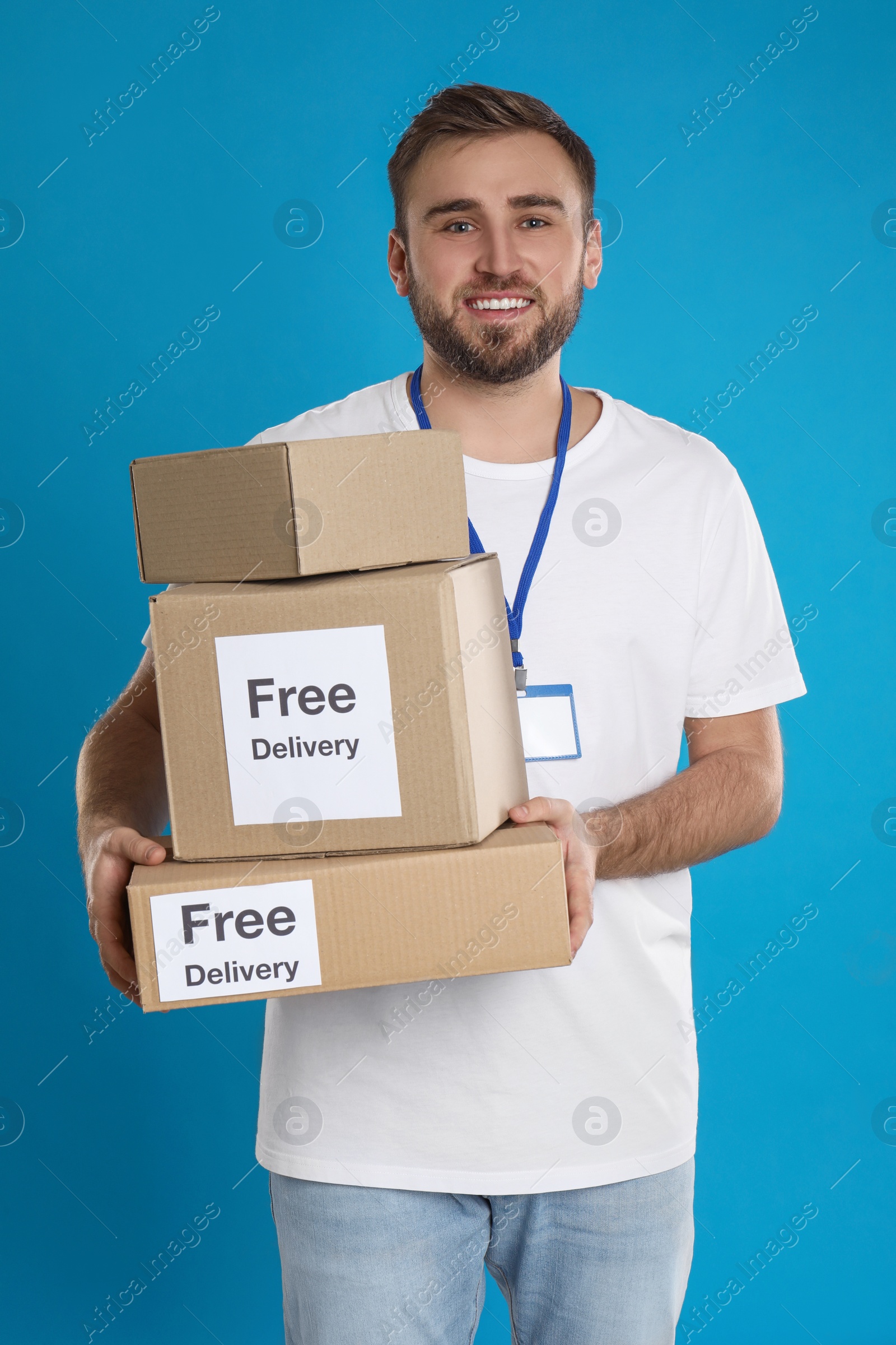 Photo of Male courier holding parcels with stickers Free Delivery on light blue background