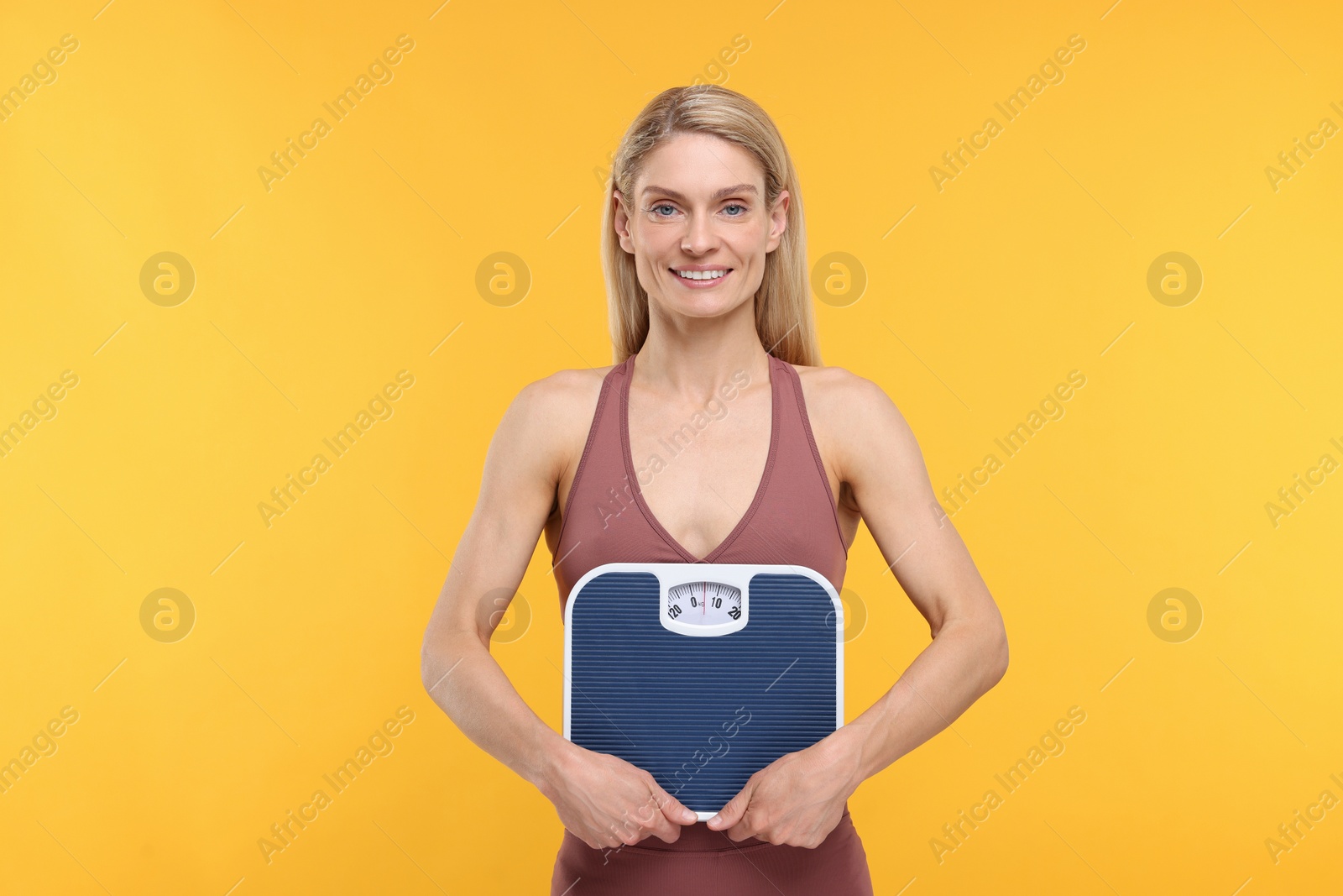 Photo of Slim woman holding scales on yellow background. Weight loss