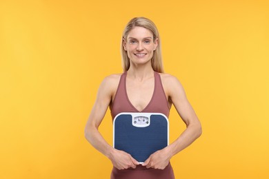 Photo of Slim woman holding scales on yellow background. Weight loss