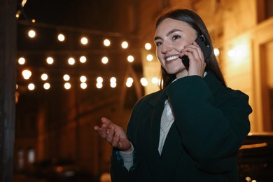 Photo of Smiling woman talking by smartphone on night city street. Space for text