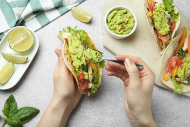 Photo of Woman adding guacamole to delicious taco at light grey table, top view