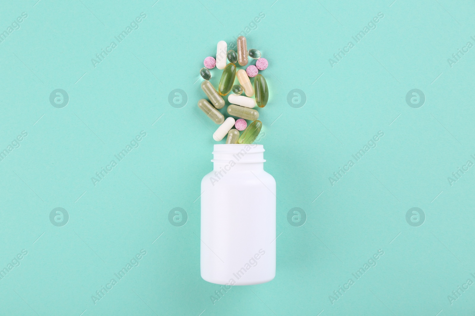 Photo of Bottle and different vitamin pills on turquoise background, top view