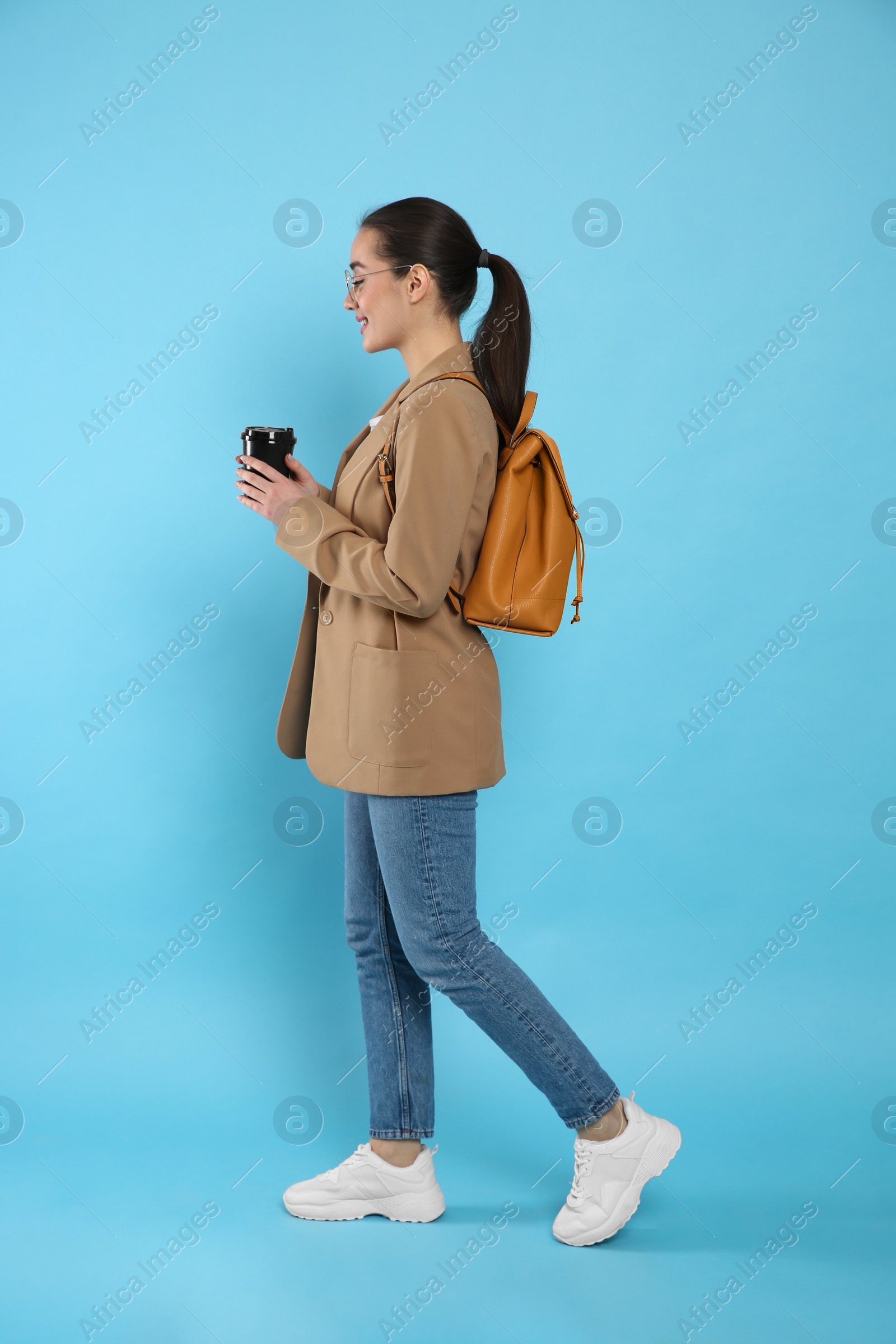 Photo of Beautiful young woman with stylish leather backpack and cup of coffee on turquoise background