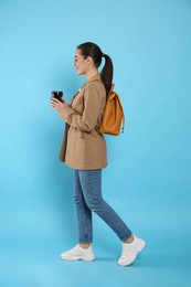 Beautiful young woman with stylish leather backpack and cup of coffee on turquoise background