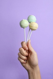 Photo of Woman holding sweet cake pops on lilac background, closeup