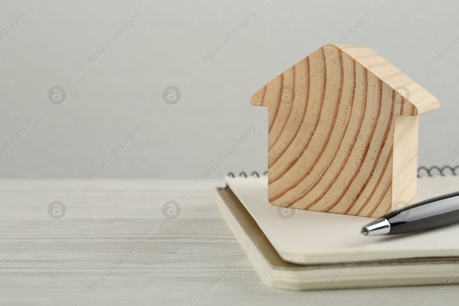 Photo of Mortgage concept. House model, notebook and pen on white wooden table, space for text