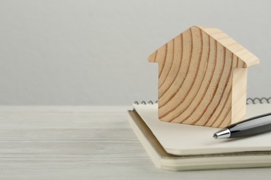 Photo of Mortgage concept. House model, notebook and pen on white wooden table, space for text
