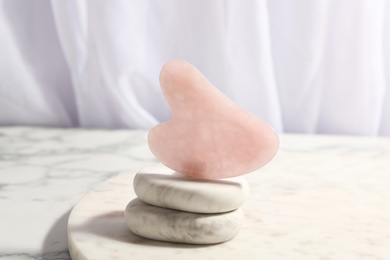 Photo of Rose quartz gua sha tool and spa stones on white marble table