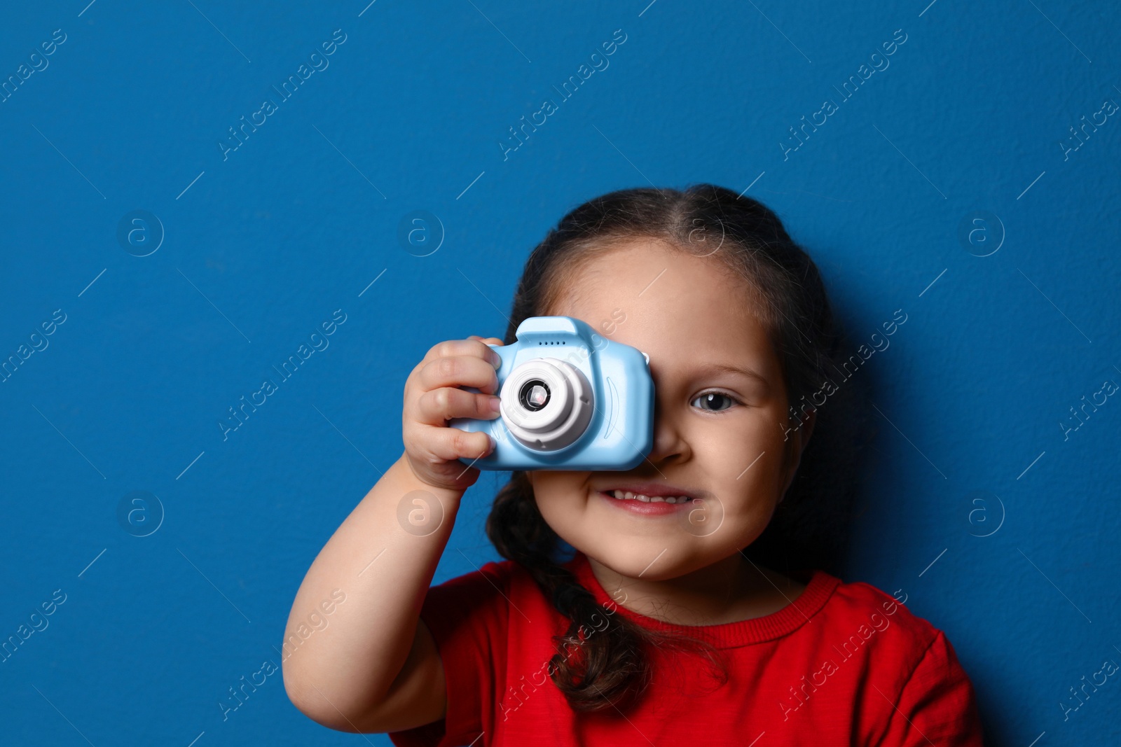 Photo of Little photographer taking picture with toy camera on blue background