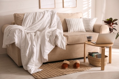 Photo of Comfortable sofa with blanket in stylish room