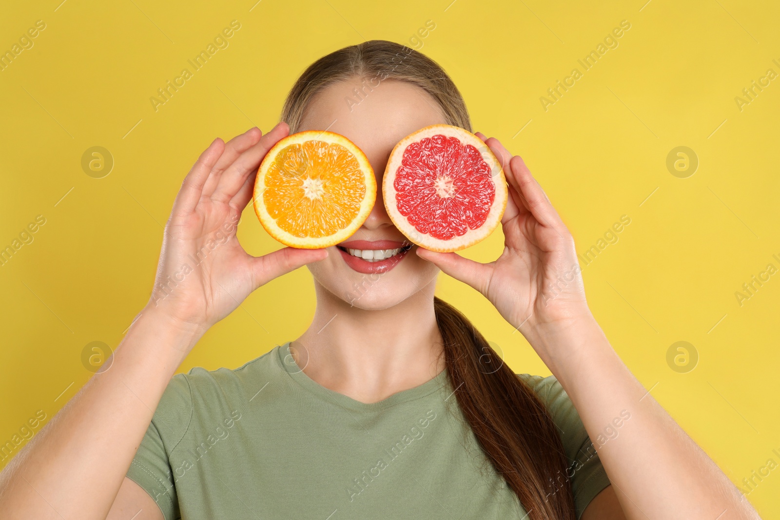 Photo of Young woman with cut orange and grapefruit on yellow background. Vitamin rich food