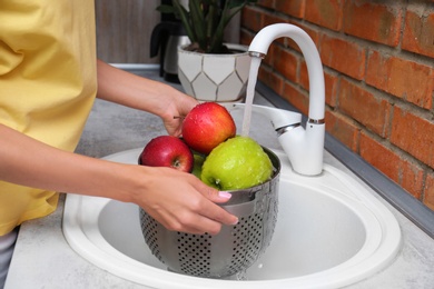 Photo of Woman washing fresh apples in kitchen sink, closeup