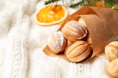 Photo of Delicious nut shaped cookies and dried orange slice on white knitted fabric, closeup. Space for text