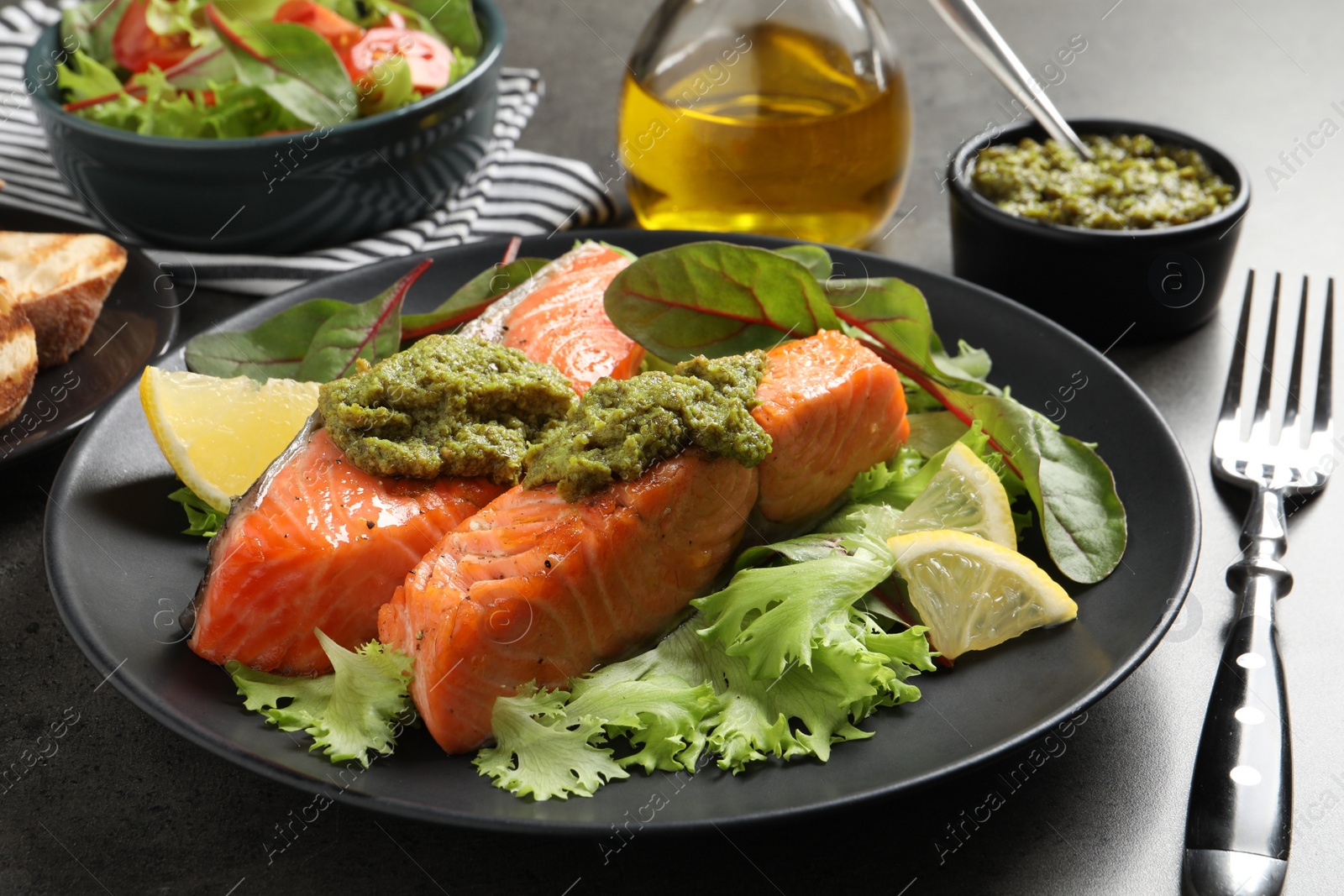 Photo of Tasty cooked salmon with pesto sauce served on dark grey table