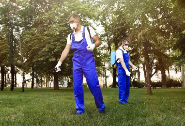 Photo of Workers spraying pesticide onto lawn outdoors. Pest control