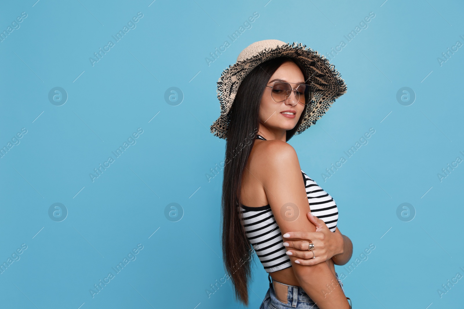 Photo of Beautiful young woman with straw hat and stylish sunglasses on light blue background. Space for text