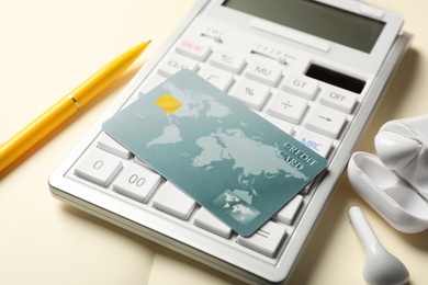 Credit card, calculator and wireless earphones on open notebook, closeup