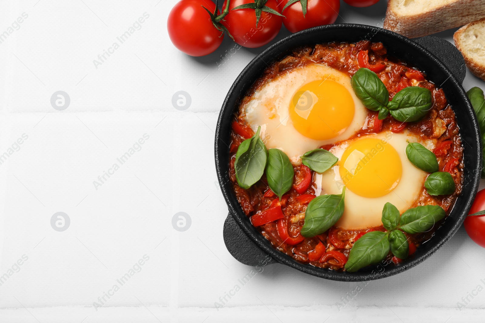 Photo of Delicious Shakshuka served on white tiled table, flat lay. Space for text