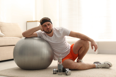 Photo of Lazy young man with sport equipment at home