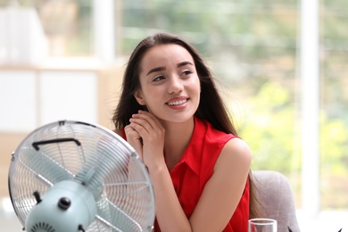 Young woman enjoying air flow from fan in office. Summer heat