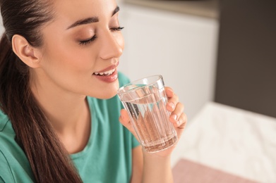 Photo of Young woman drinking pure water from glass indoors, closeup