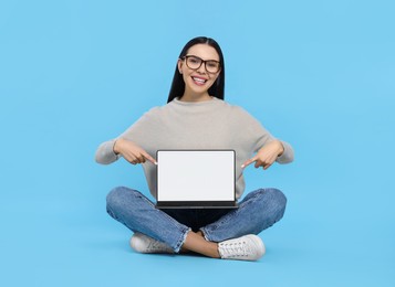 Happy woman pointing at laptop on light blue background