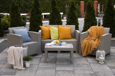 Beautiful rattan garden furniture, soft pillows and different decor elements in backyard