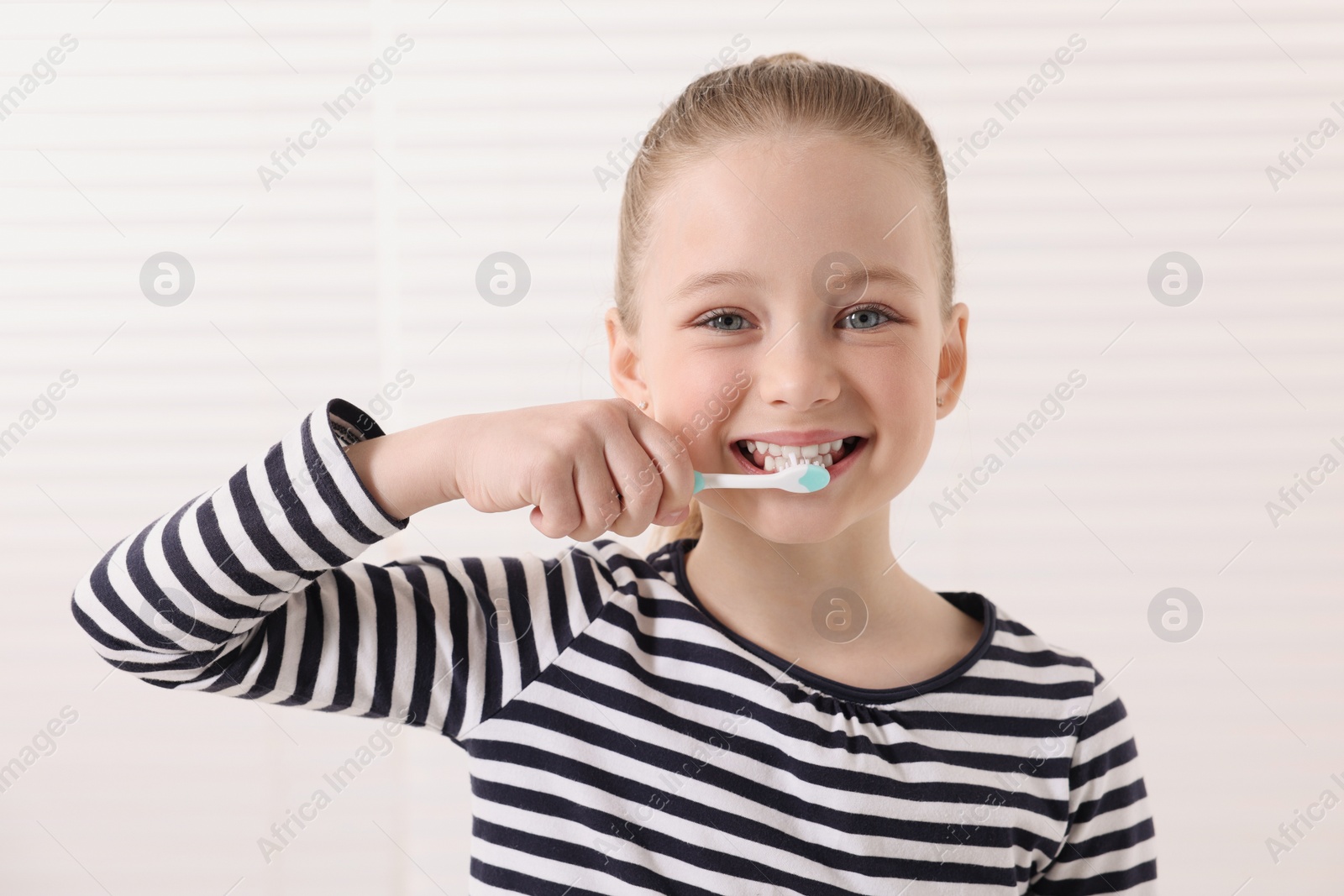 Photo of Cute little girl brushing her teeth with plastic toothbrush on white background