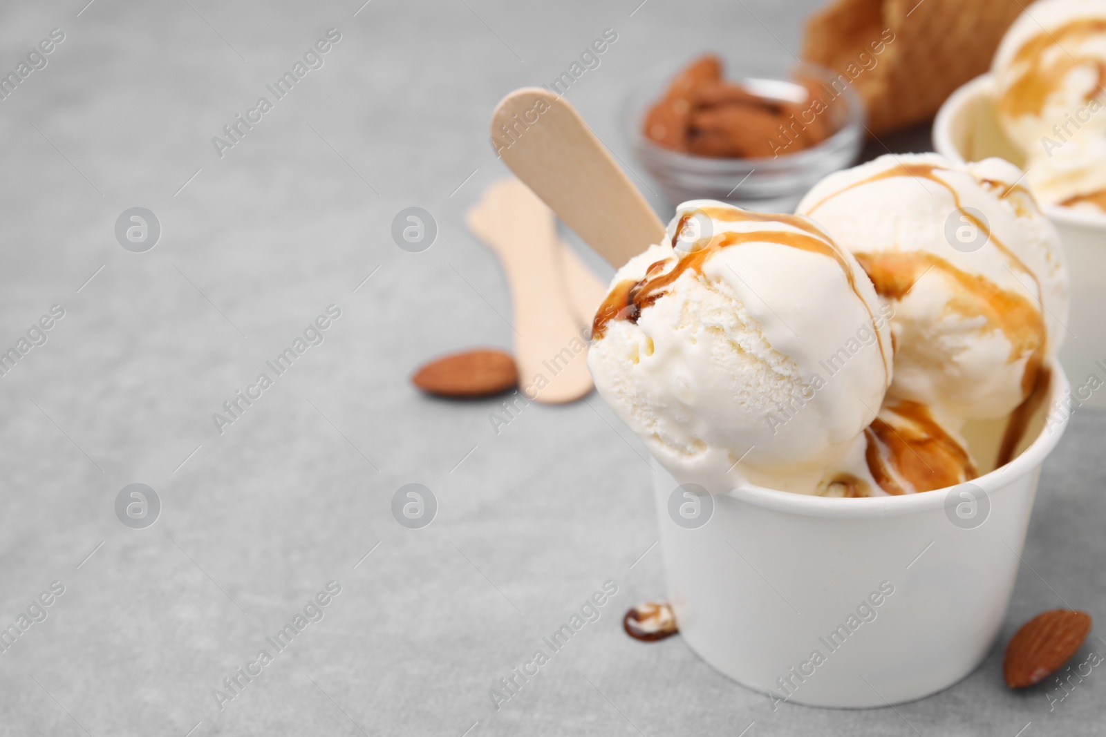 Photo of Scoops of ice cream with caramel sauce in paper cup on light grey table, closeup. Space for text