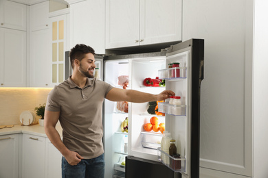 Photo of Young man taking yoghurt out of refrigerator in kitchen