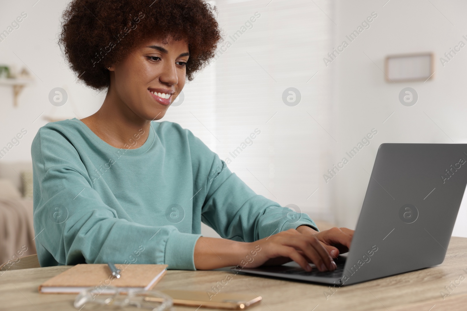 Photo of Young woman using laptop at wooden desk in room