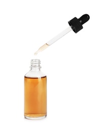 Essential oil dripping from pipette into glass bottle on white background