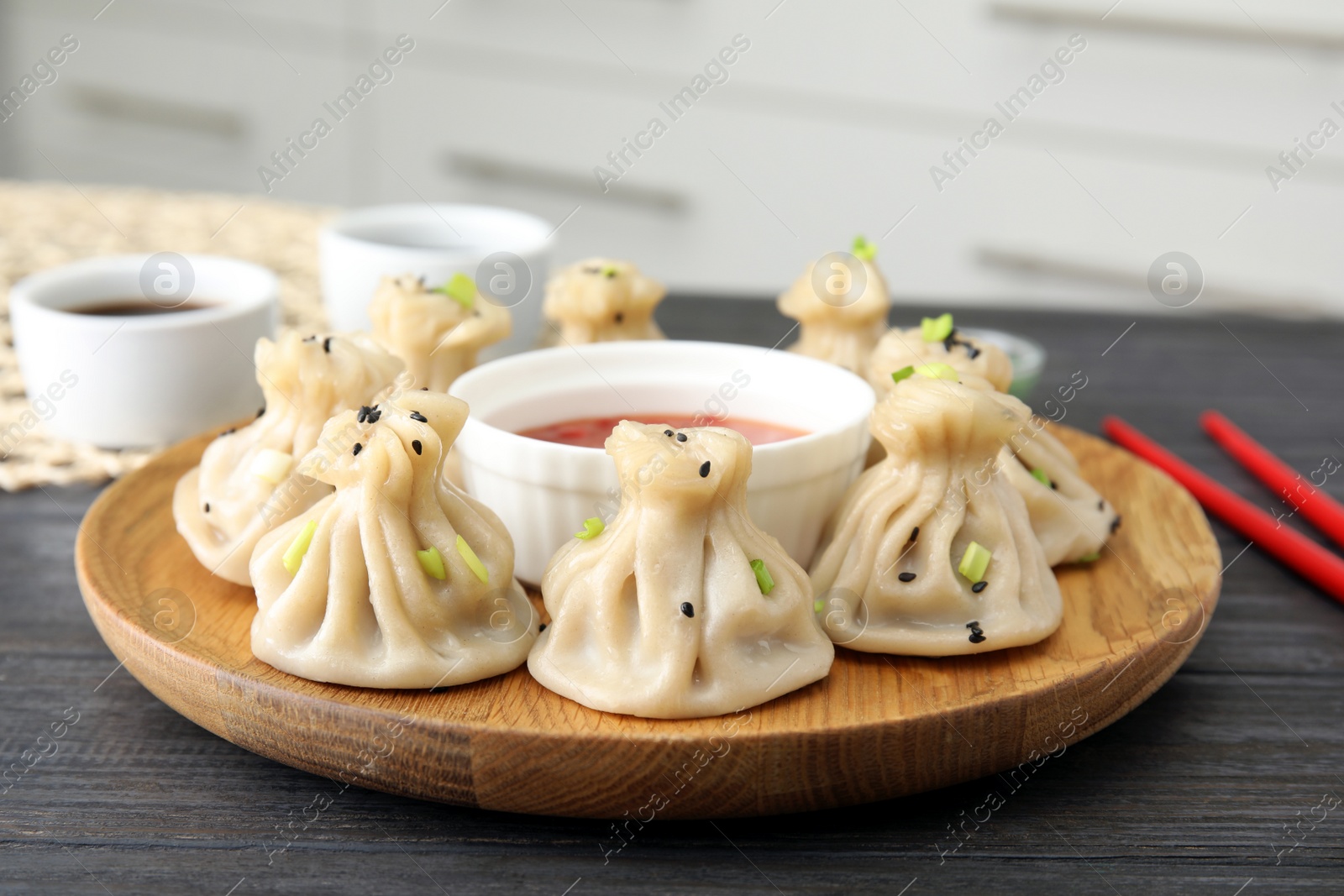 Photo of Wooden plate with tasty baozi dumplings and sauce on table