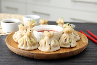 Photo of Wooden plate with tasty baozi dumplings and sauce on table