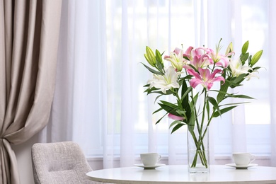 Photo of Vase with bouquet of beautiful lilies on white table indoors. Space for text