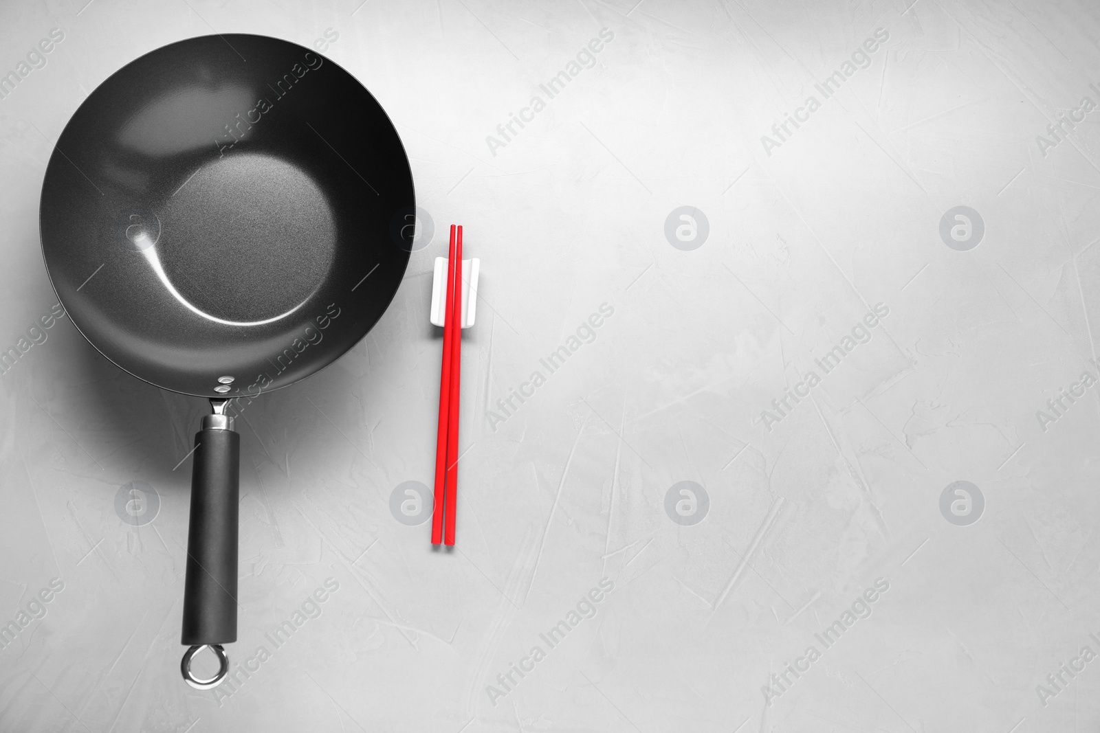 Photo of Empty wok and chopsticks on grey table, flat lay. Space for text