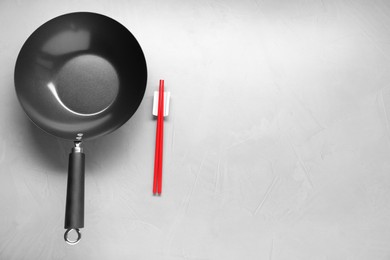 Empty wok and chopsticks on grey table, flat lay. Space for text