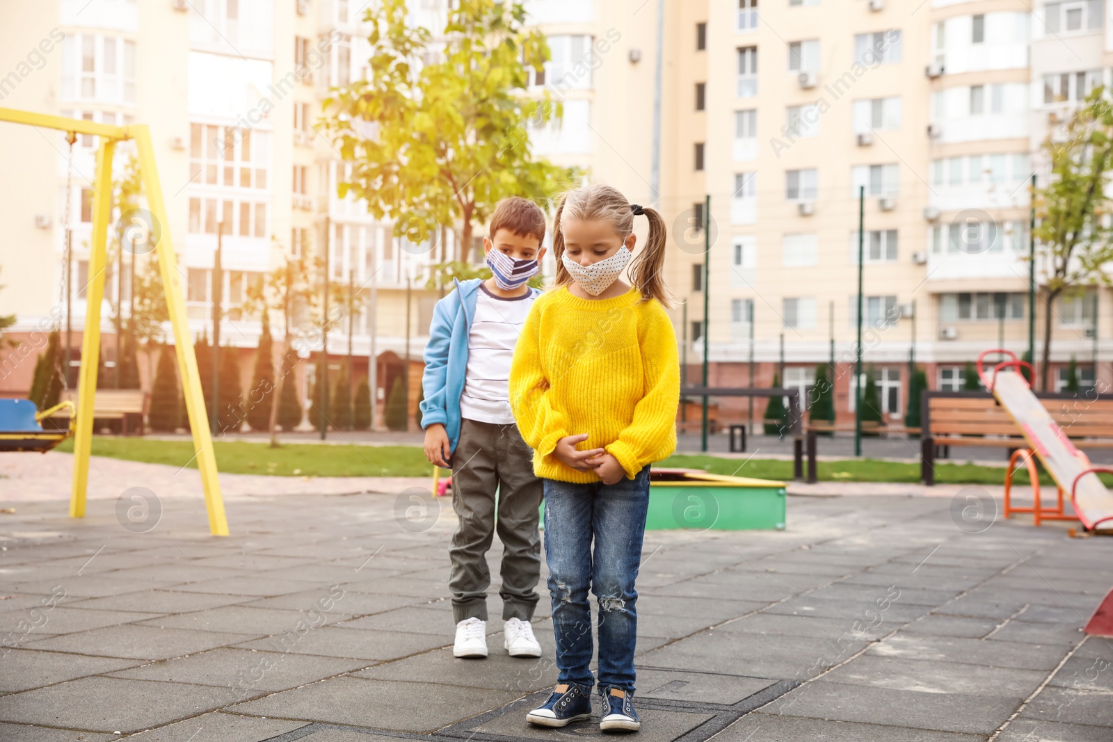 Photo of Little children with medical face masks on playground during covid-19 quarantine