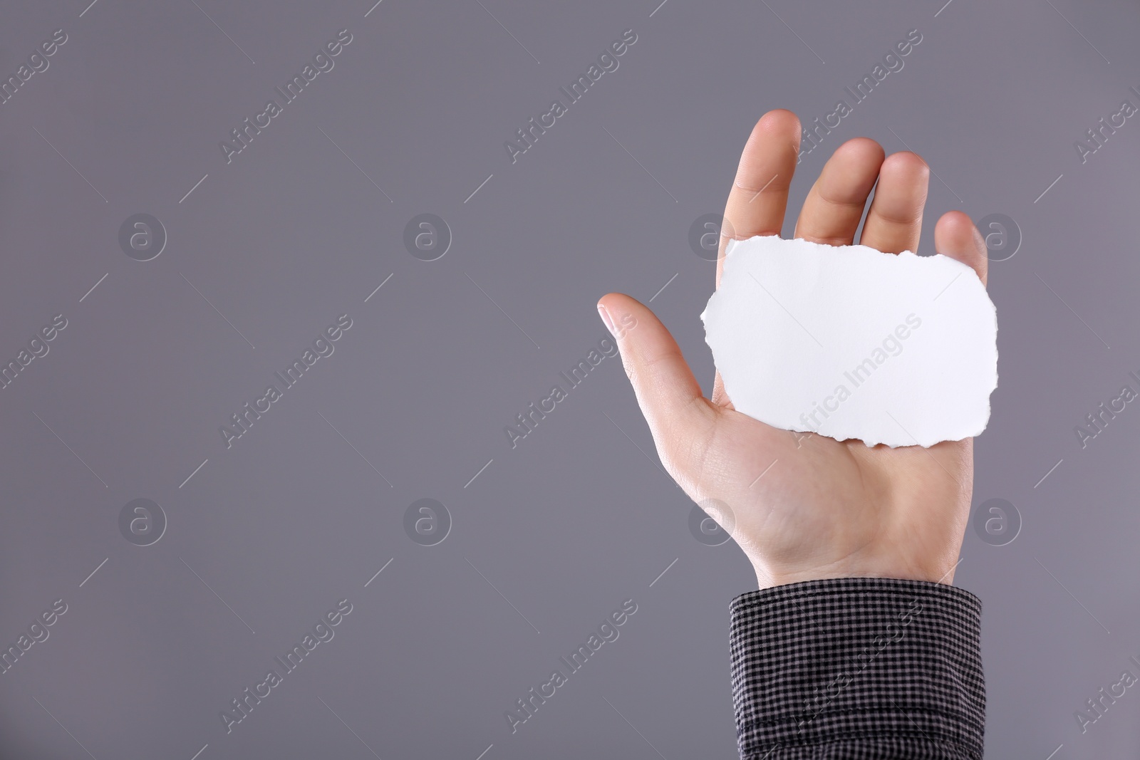 Photo of Man holding sheet of torn paper on grey background, closeup. Mockup for design