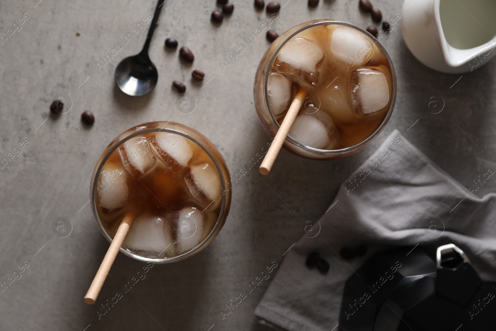 Photo of Refreshing iced coffee with milk in glasses, ingredients and spoon on gray table, flat lay