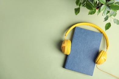Modern headphones with hardcover book on green background, top view. Space for text