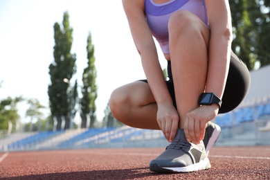 Photo of Woman with fitness tracker tying shoelaces at stadium, closeup